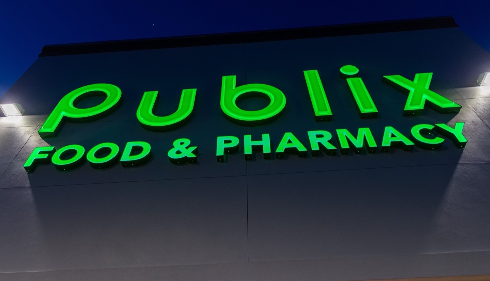 A lighted green Publix Food and Pharmacy sign on a store at dusk