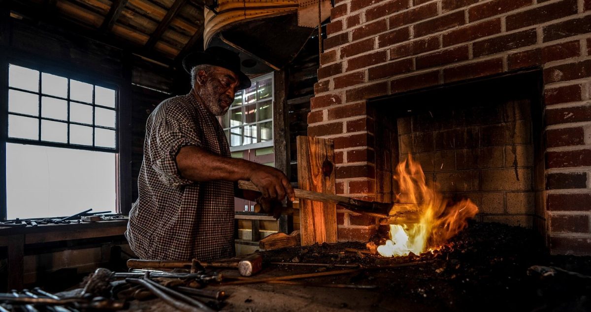 A blacksmith at Historic Westville heats iron over a coal forge.