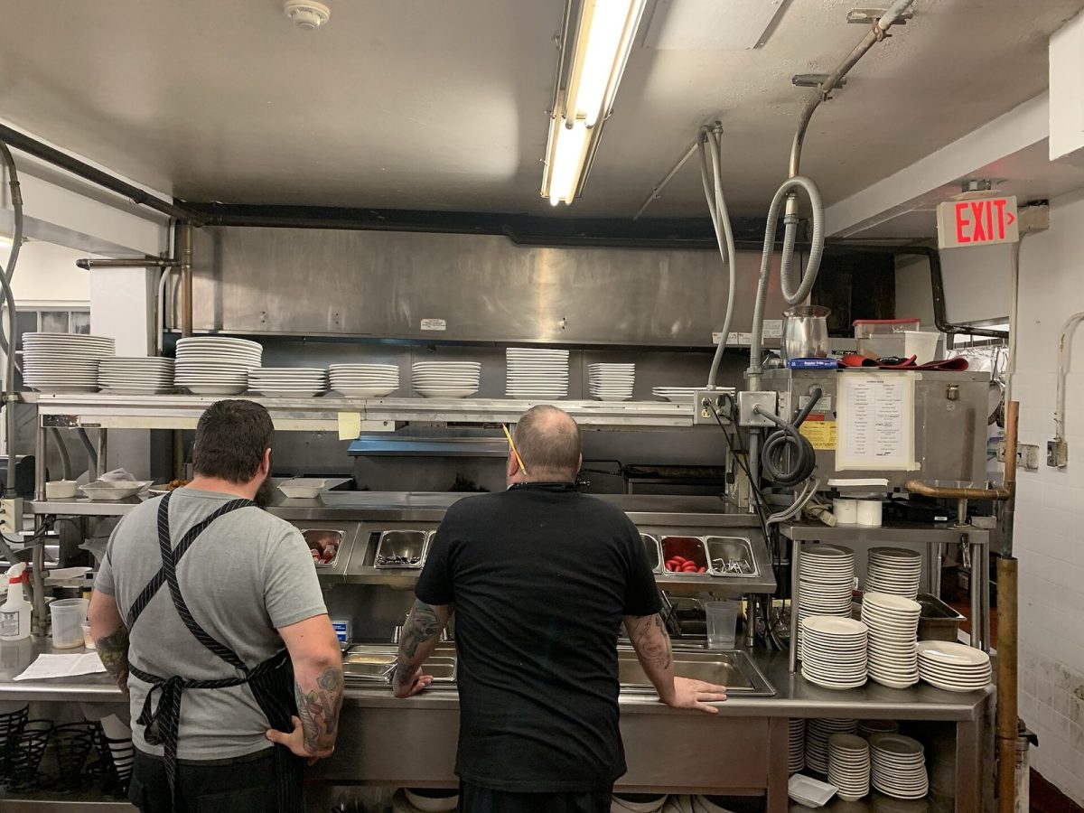 Kitchen workers stand at the dish and expo station of a restaurant kitchen, with stacks of plates on the shelves above (file photo).